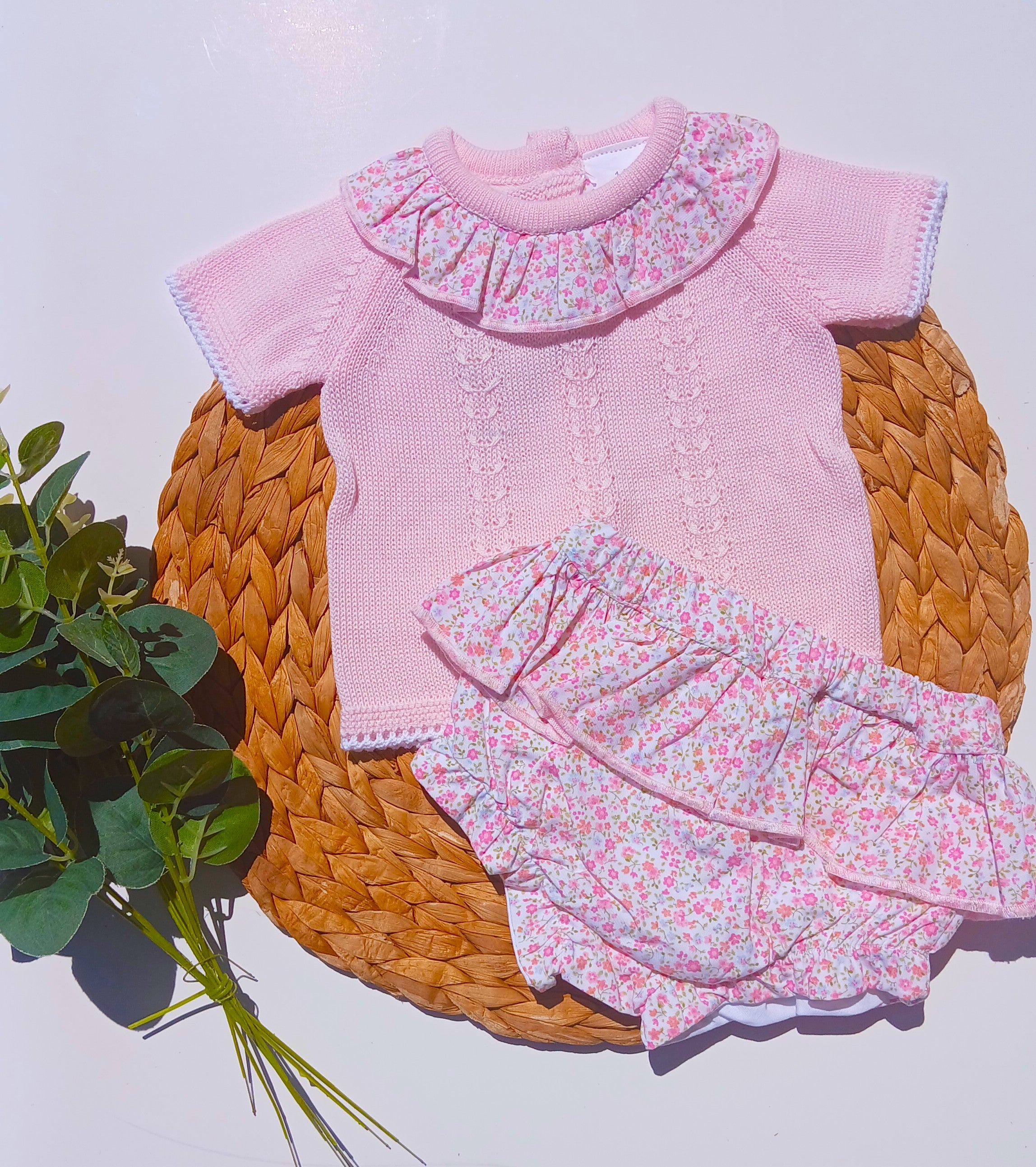 Pink baby outfit with floral details on a woven mat