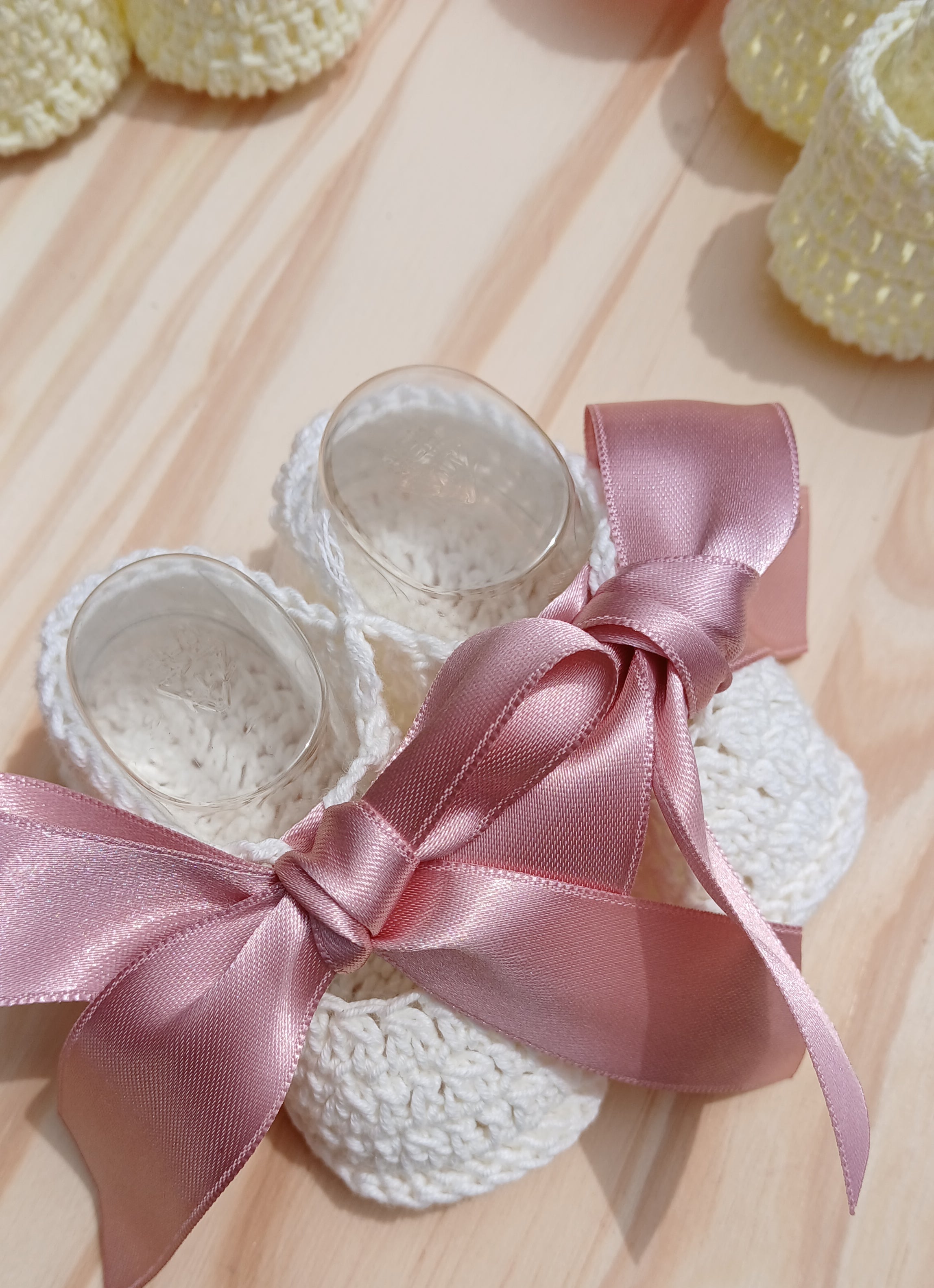 White crocheted baby booties with a pink satin ribbon on a wooden surface