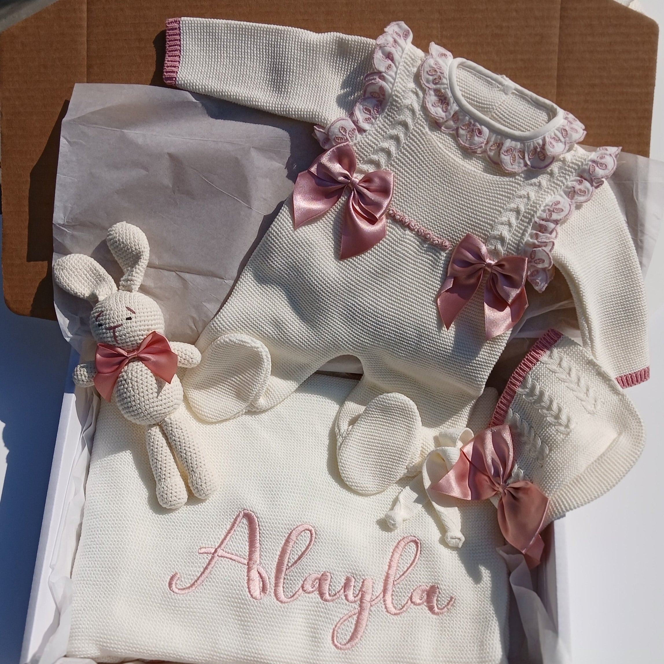 Baby outfit with floral details and a teddy bear in a box labeled 'Alayla'.