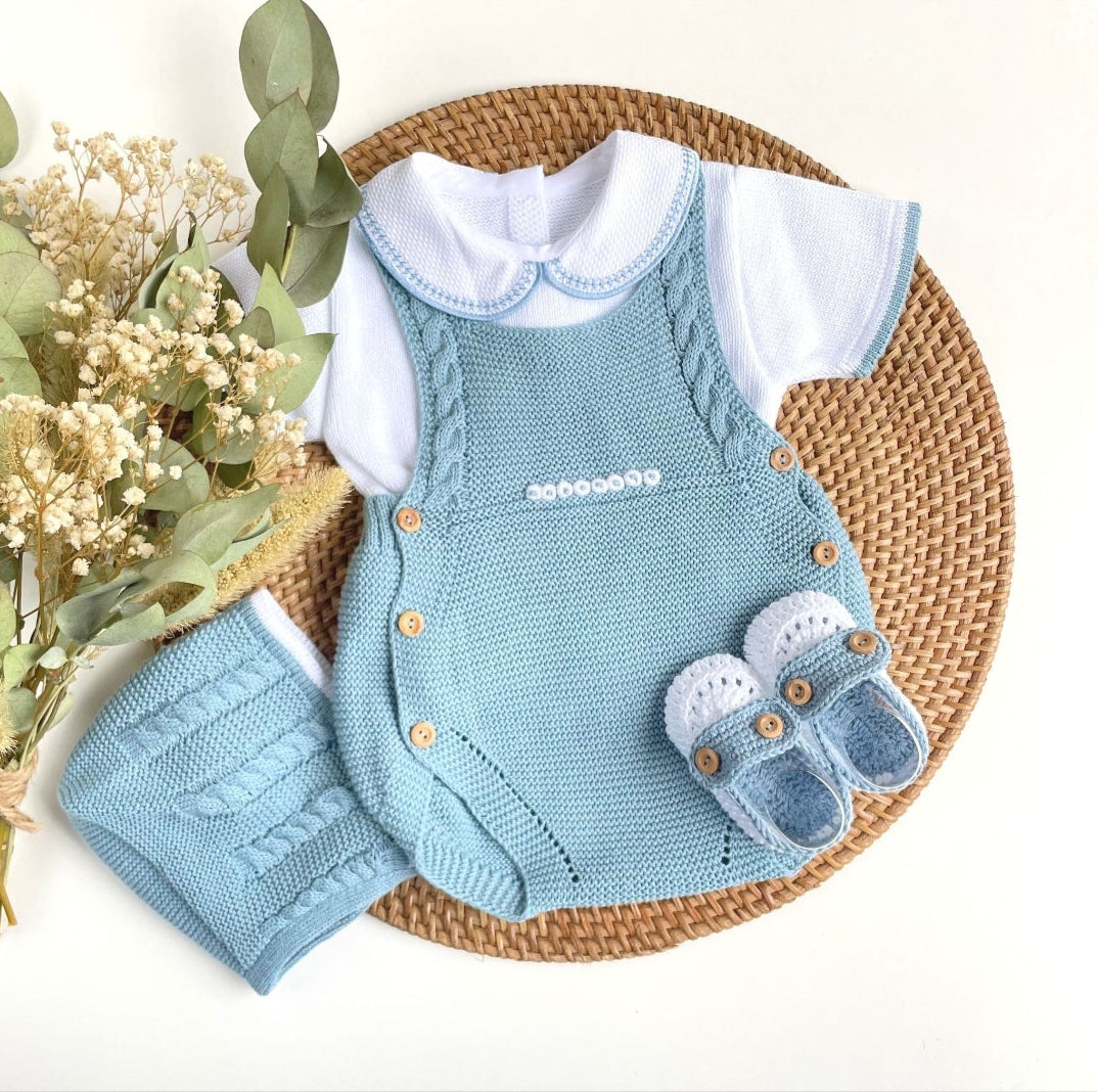 A complete four-piece knitted baby outfit in indigo blue, including a top, bottom, bonnet, and bootie, 