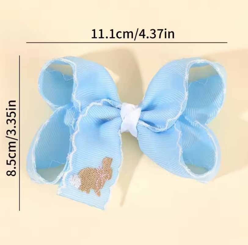 Light blue hair bow with a small embroidered design on a beige background