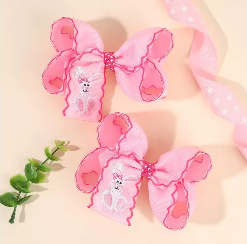 Two pink butterfly-shaped hair accessories with embroidered faces on a beige background. white Easter bunny embroidered