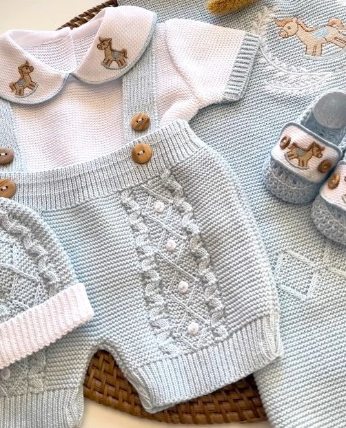 Knitted baby outfit with romper, cardigan, and shoes on a textured surface.