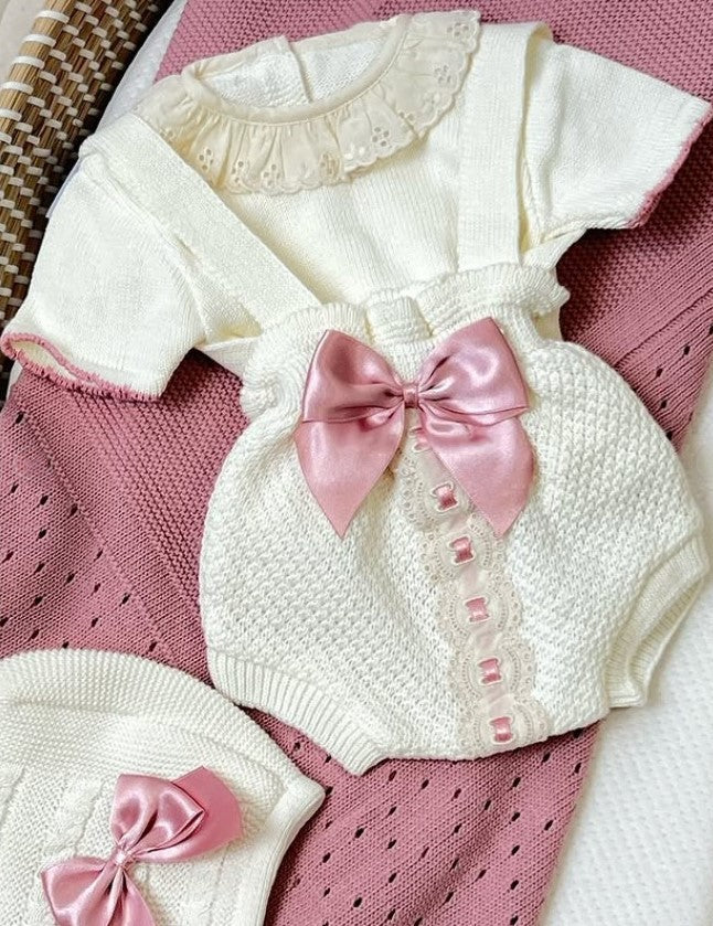 White baby outfit with pink bows on a pink textured surface