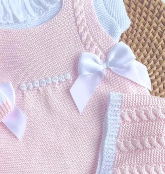 Close-up of a pink dress with white bow and lace details on a woven surface.