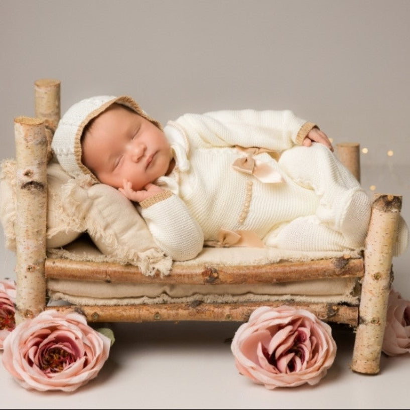 Newborn baby in a small wooden bed with pink flowers on a neutral , newborn knit going home outfit, newborn baby girl coming home knit outfit 