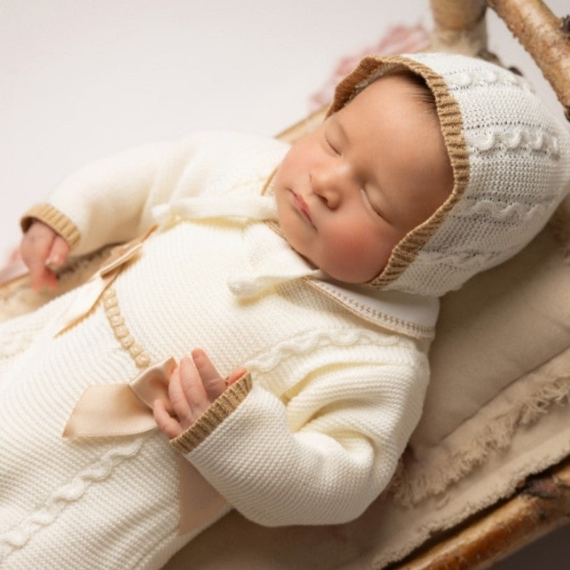 Newborn baby in a white knitted outfit and hat lying on a wooden surface. ,newborn knit going home outfit, newborn baby girl coming home knit outfit