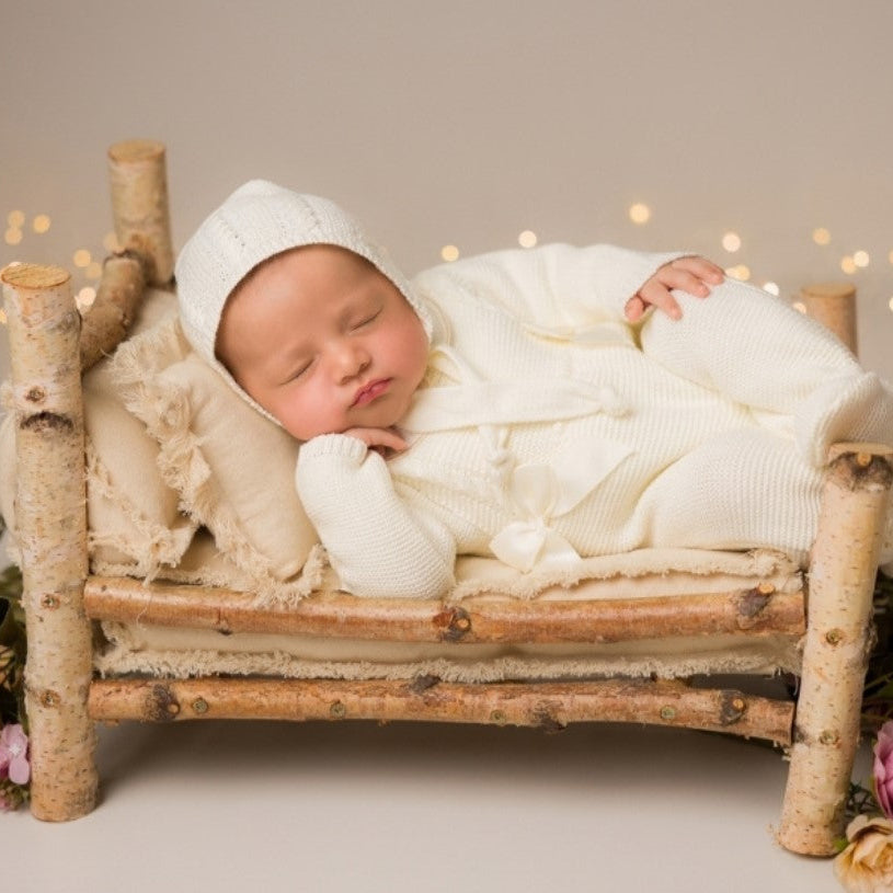 , newborn knit going home outfit, newborn baby girl coming home knit outfit . Newborn baby in a small wooden bed with white bedding, surrounded by flowers and lights.