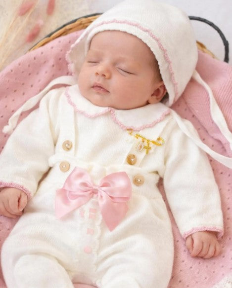 Newborn baby in a white outfit with pink accents on a pink blanket