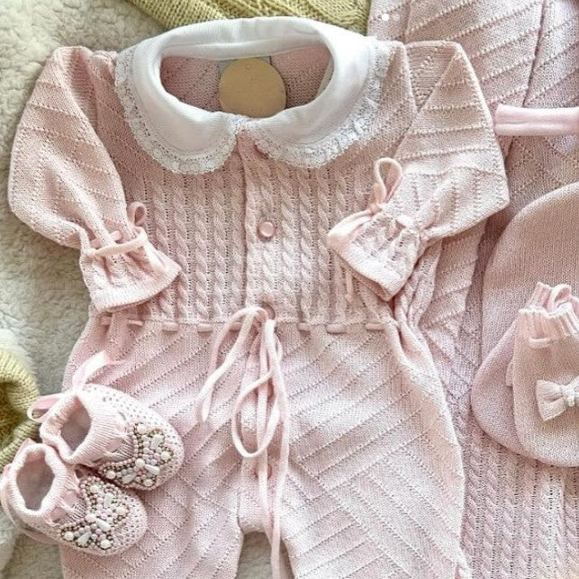 Pink baby outfit set with cardigan, romper, shoes, and hat on a soft surface.