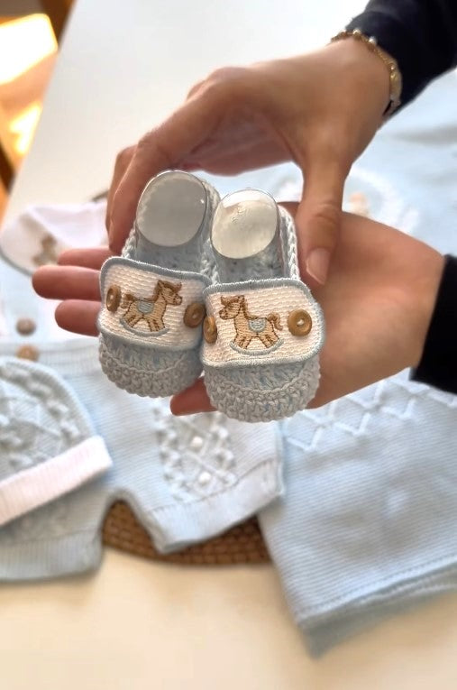 Baby booties with horse design held by a person, with a blurred background