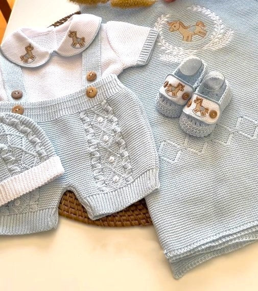 Knitted baby outfit with hat, romper, and shoes on a textured surface