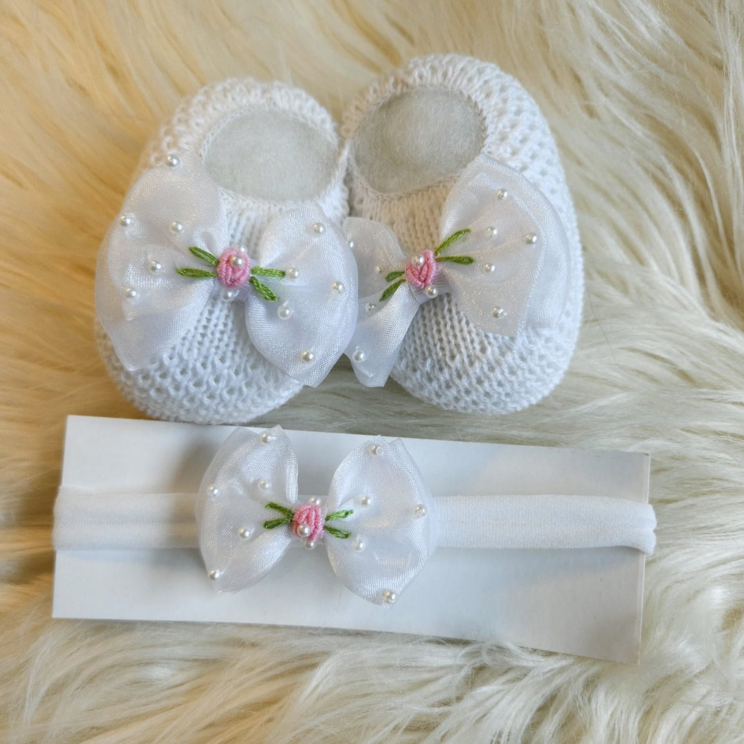 White baby shoes and headband with floral decorations on a fluffy white surface