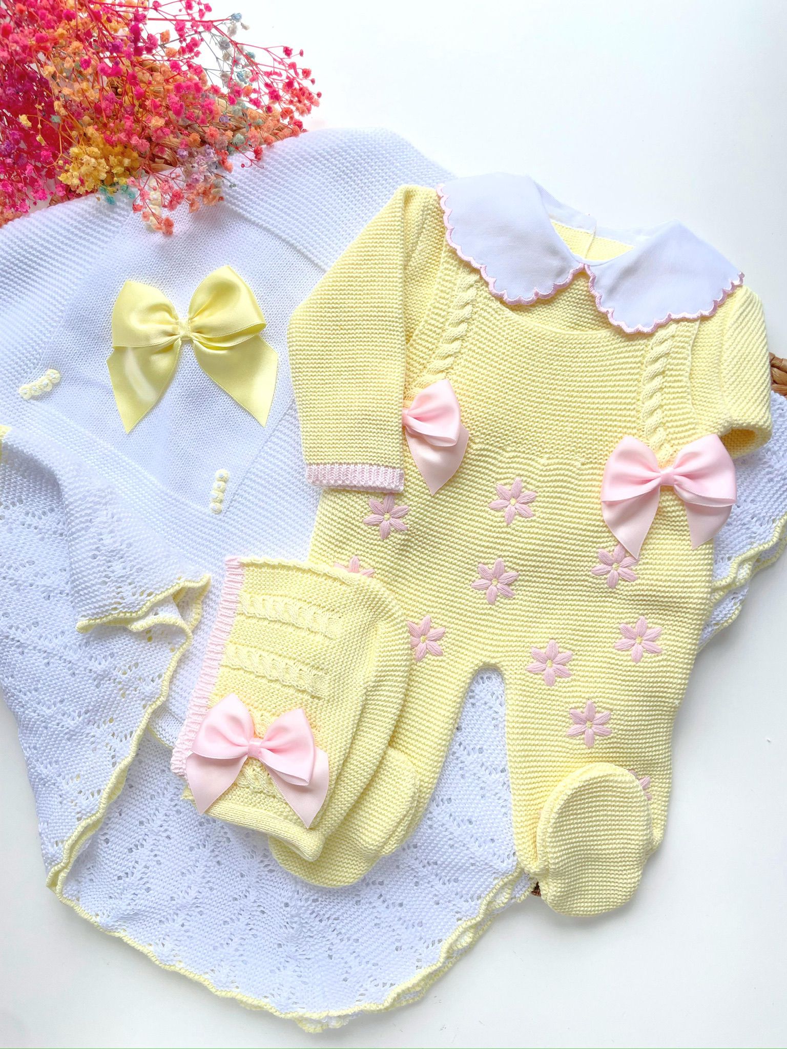 Yellow baby romper with pink bows on a white blanket