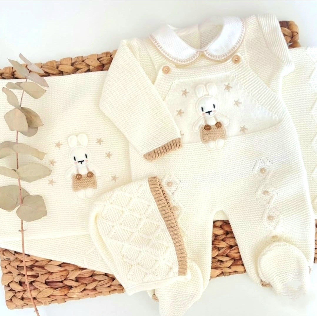 Newborn bunny coming home outfit. Baby outfit with white sweater, pants, and hat on a woven basket with eucalyptus leaves.