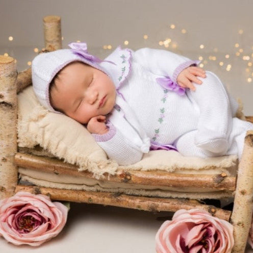 Newborn baby in a small bed with pink flowers and a soft background newborn girl knit going home outfit with flowers embroidered details 
lilac cetin. Baby girl knit coming home outfit in white details in lilac, collar with handmade flowers
purple newborn girl outfit