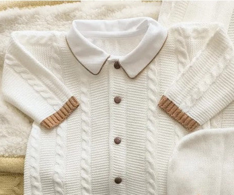 Knitted baby outfit with white sweater, pants, and hat on a soft surface