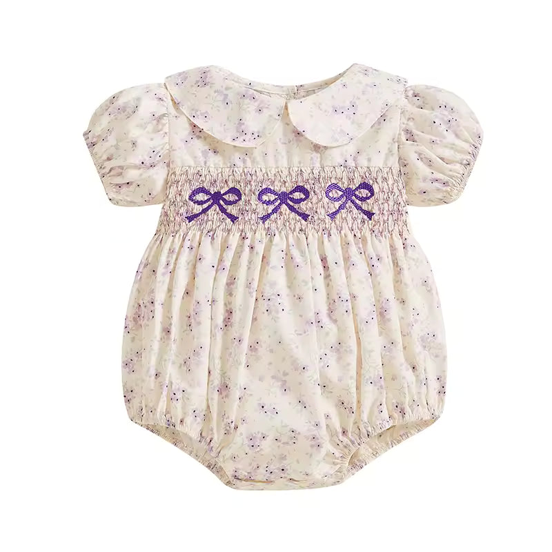 Baby romper with floral pattern and purple bows on a white background