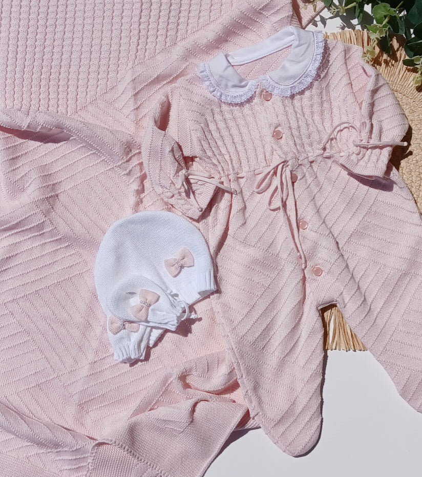 Pink baby outfit with matching bonnet on a textured surface
