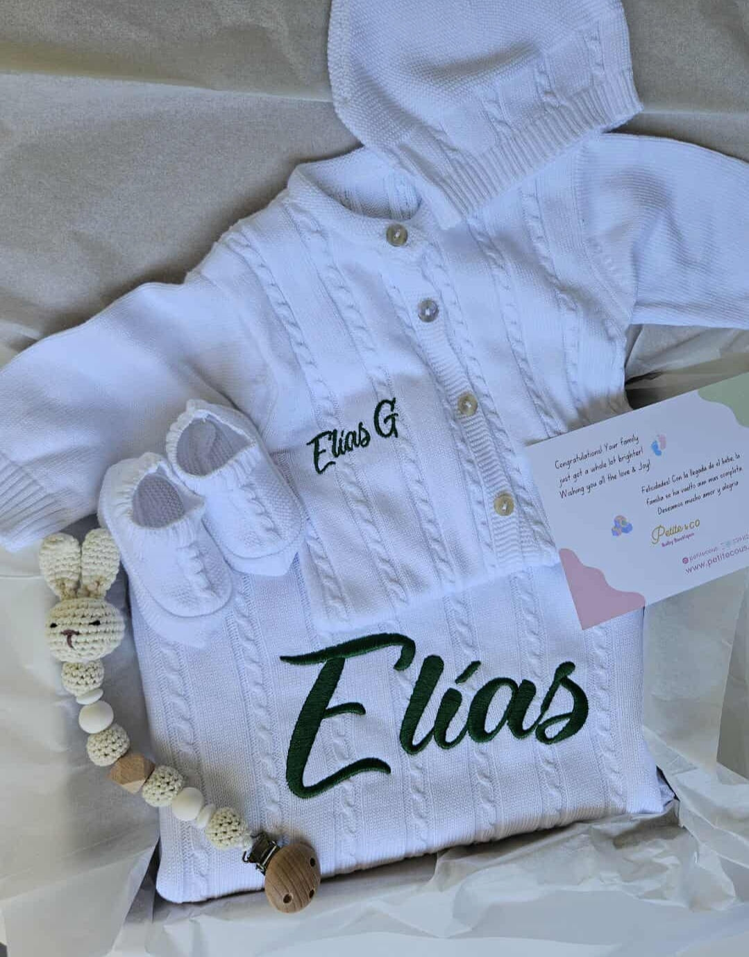 White baby jacket with 'Elias' embroidered on it, lying on a light-colored surface.