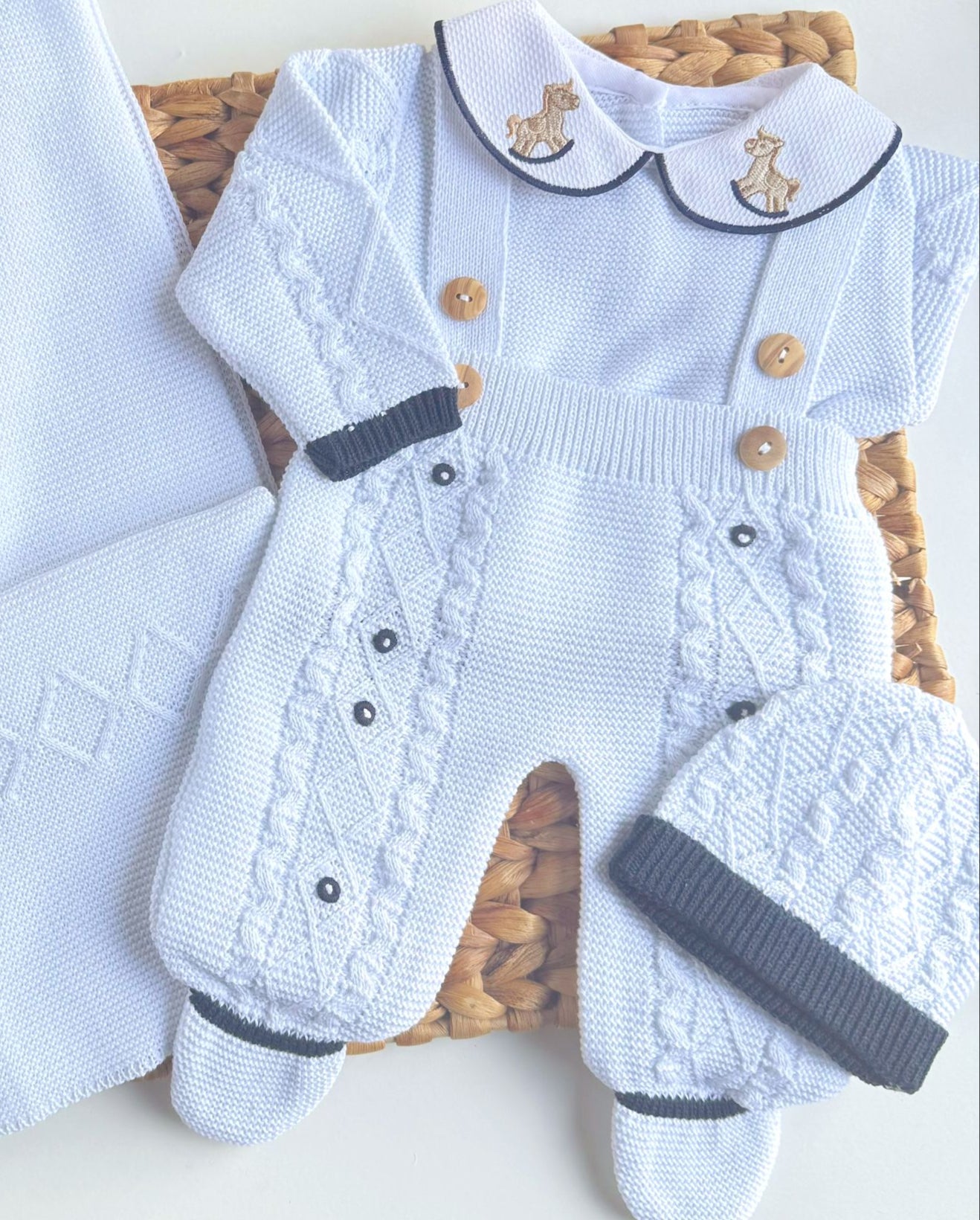 Baby outfit with overalls, hat, and blanket featuring a brand logo on a white surface. rocking horse on the collar