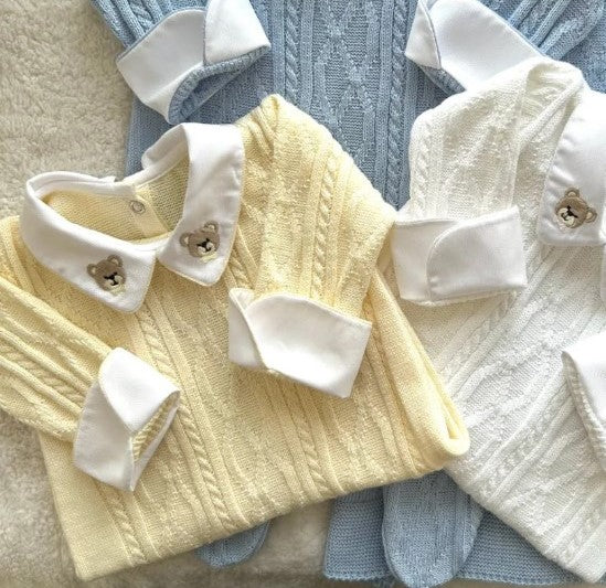 Two baby knit long-sleeve sweaters with white collar and cuff details, one pale yellow and one white, laid flat on top of a light blue cable-knit sweater.