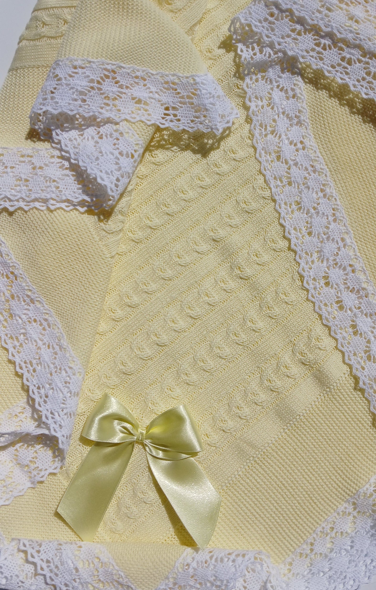 Yellow textured fabric with white lace trim and a yellow bow on a white background neutral baby blanket 